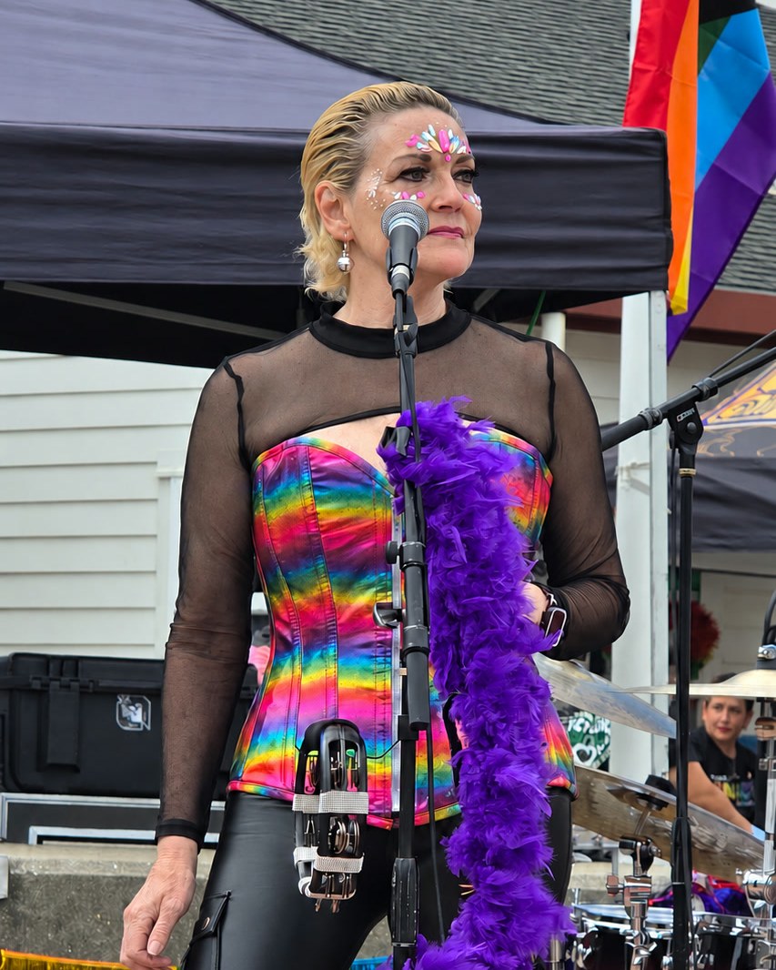 Vocalist in a rainbow sequin top and purple feather boa at a festival